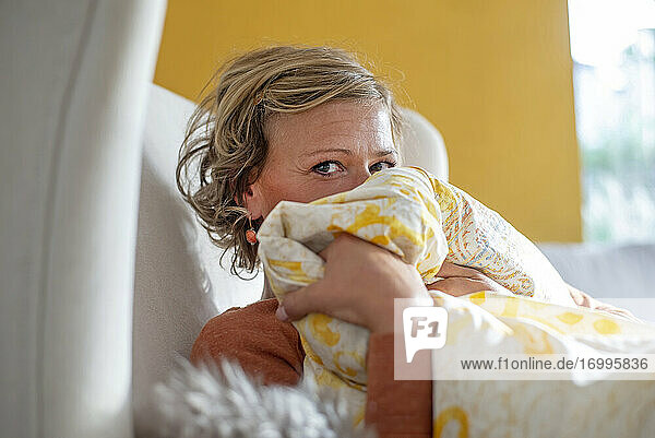 Frau bedeckt ihr Gesicht mit einer Decke  während sie zu Hause auf dem Sofa sitzt