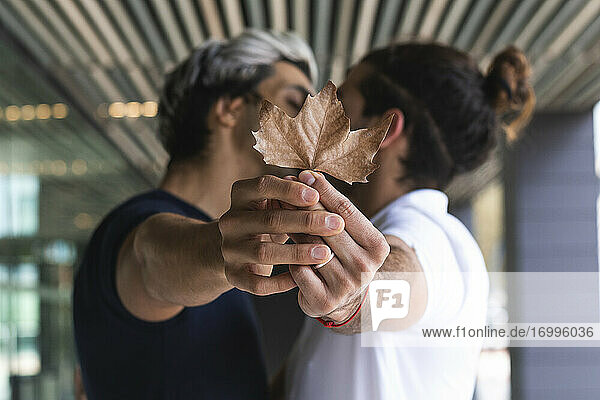 Homosexual couple showing maple leaf while kissing in city