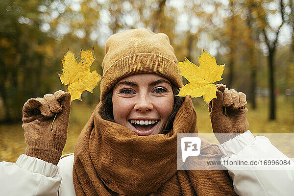 Cheerful young woman with autumn leafs in public park