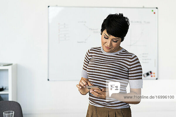 Porträt einer Geschäftsfrau im Büro stehend mit Smartphone in den Händen