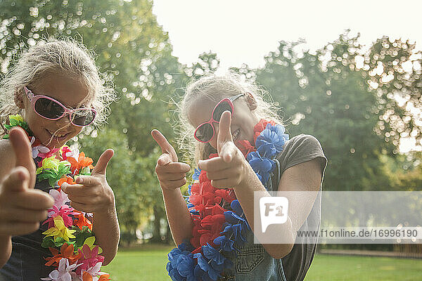 Fröhliche Mädchen mit Sonnenbrillen und Blumengirlanden in einem öffentlichen Park