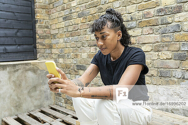 Woman using mobile phone while sitting against wall at back yard
