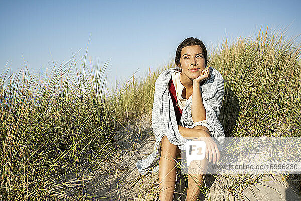 Nachdenkliche Frau mit Hand am Kinn  die wegschaut  während sie am Strand sitzt
