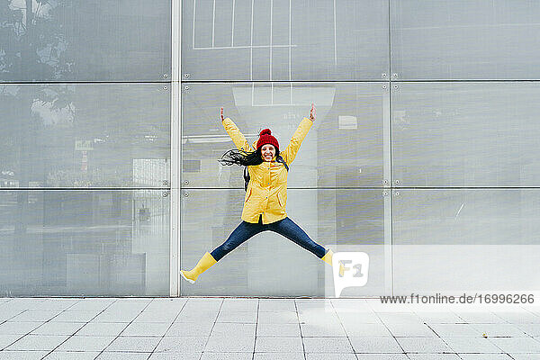 Smiling woman jumping with hand raised on footpath against building exterior