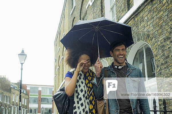 Fröhliches Paar mit Regenschirm beim Spaziergang in der Stadt