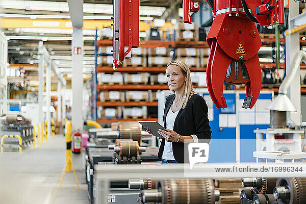 Blond female entrepreneur looking away while holding digital tablet at factory