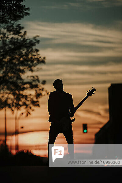 Silhouette of musician playing bass guitar while standing on road
