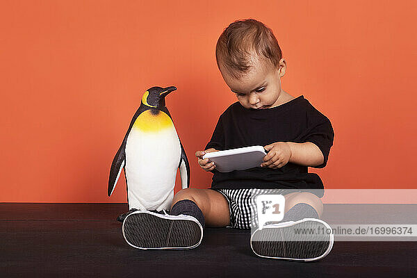 Baby-Mädchen  das Spielzeug ignoriert  während es ein Mobiltelefon benutzt  das vor einem orangefarbenen Hintergrund sitzt
