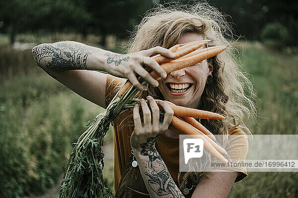 Female farmer smiling while holding carrots at farm