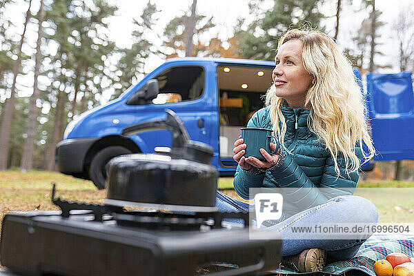 Blonde Frau hält Teetasse und träumt beim Camping in Cannock Chase vor sich hin