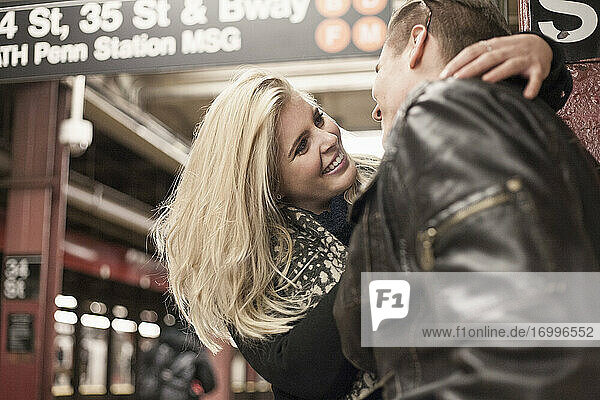 Smiling girlfriend embracing boyfriend while standing at subway station