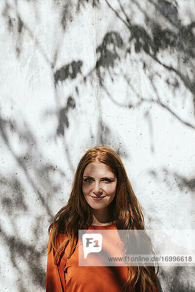 Junge Frau lächelt  während sie vor einer Baumschattenwand steht