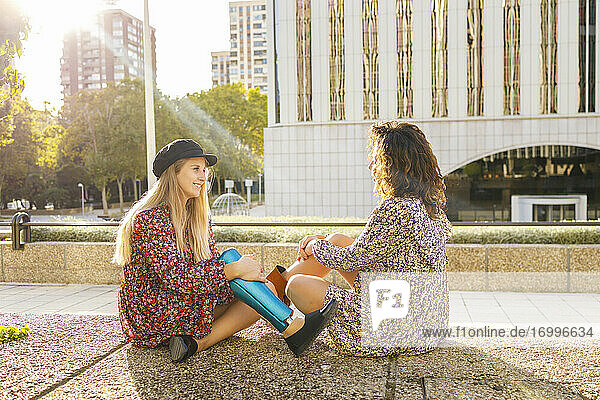 Junge Frau mit Beinprothese sitzt mit einer Freundin auf einem Fußweg in der Stadt