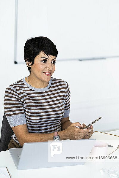 Portrait of businesswoman sitting at office desk with smart phone in hands