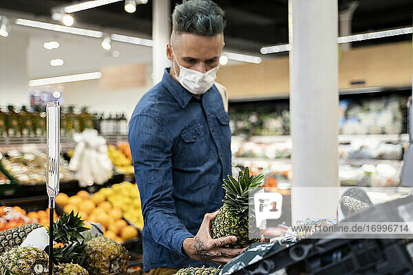 Mid adult man wearing face mask buying pineapple in supermarket