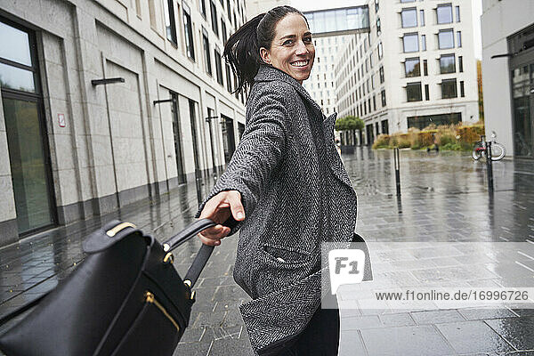 Glückliche Geschäftsfrau  die beim Gehen auf dem Fußweg ihre Handtasche dreht