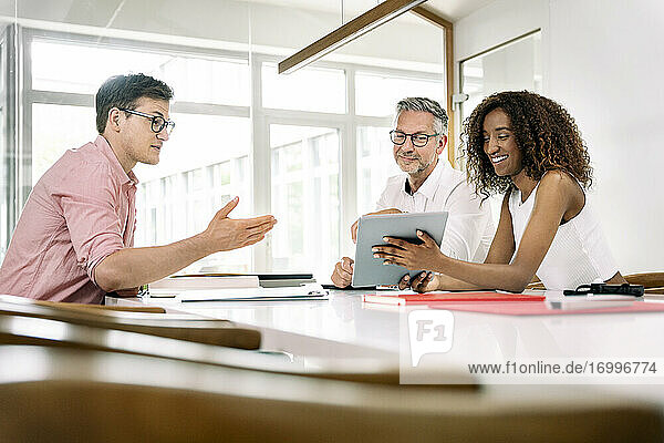 Smiling businesswoman showing digital tablet to colleagues during meeting in office