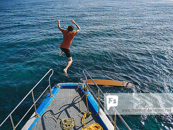 Abenteuerlustiger Mann  der an einem sonnigen Tag vom Bootsdeck springt  um zu surfen