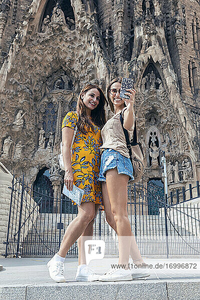 Lächelnde Freunde machen ein Selfie mit dem Handy  während sie vor der Sagrada Familia in Barcelona  Katalonien  Spanien stehen