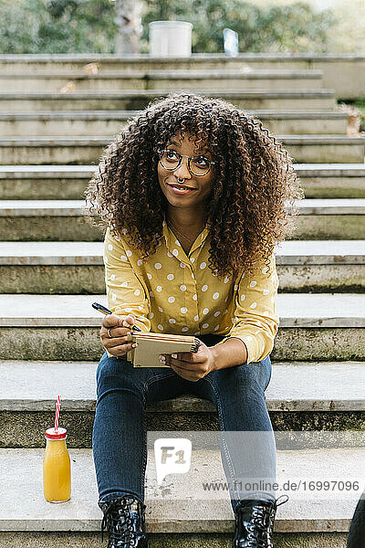 Thoughtful woman with book looking up while sitting on steps