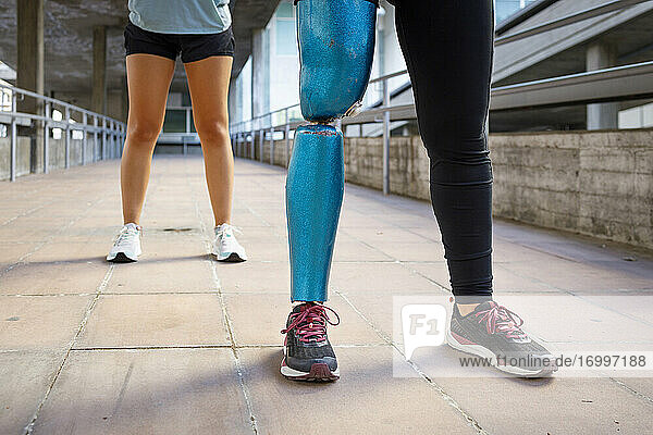 Sportswoman with prosthetic leg standing with friend on bridge