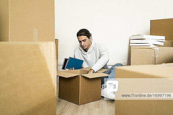 Junger Mann beim Auspacken einer Kiste während des Umzugs in eine neue Wohnung