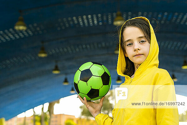 Portrait of little girl wearing yellow hooded jacket holding soccer ball
