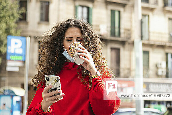 Geschäftsfrau  die ein Mobiltelefon benutzt  während sie während der COVID-19 einen Kaffee trinkt