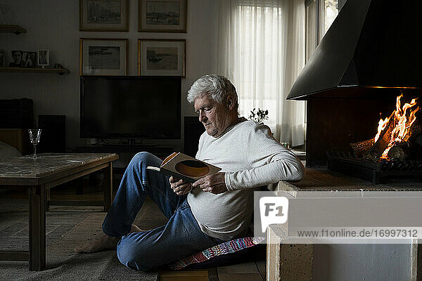 Senior man reading book while sitting on floor at home