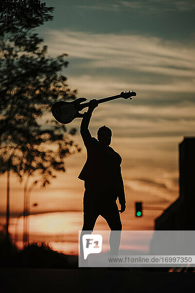 Musiker hält Bassgitarre  während er bei Sonnenuntergang auf der Straße steht