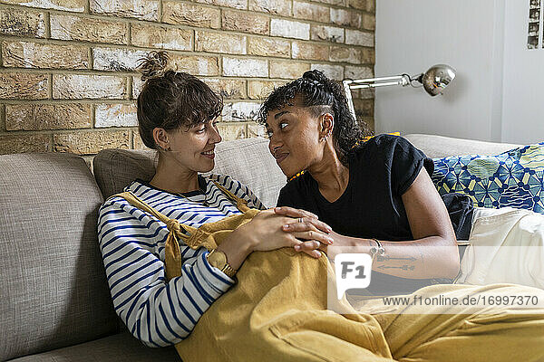 Smiling lesbian couple sitting with hands clasped on sofa at home