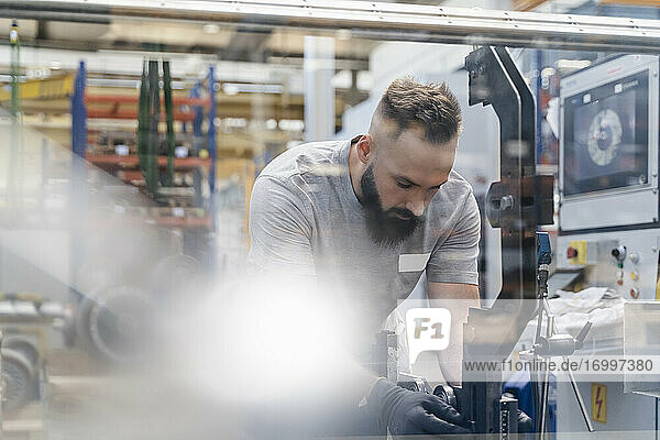 Mittlerer erwachsener männlicher Techniker  der eine Maschine in einer beleuchteten Industrieanlage untersucht