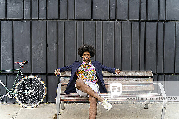 Stilvoller Mann mit Fahrrad auf einer Bank sitzend