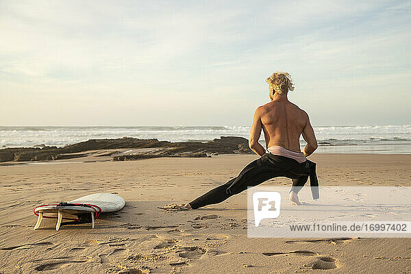 Männlicher Surfer ohne Hemd  der sich auf einem Surfbrett am Strand ausstreckt