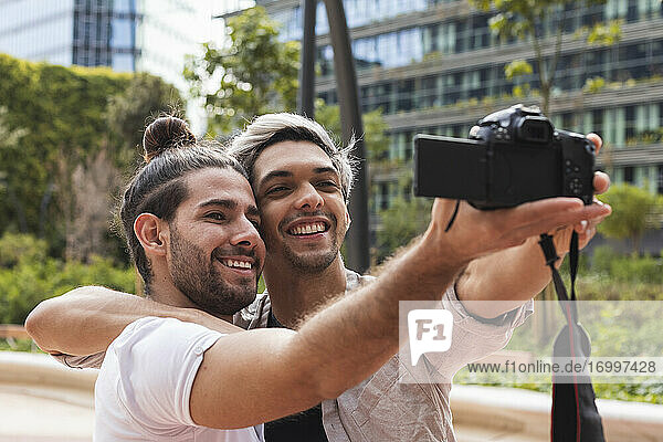 Smiling gay couple photographing through camera in city