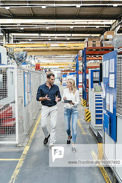 Male entrepreneur discussing while female colleague listening to him walking in factory