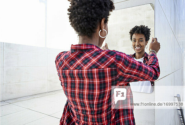 Lächelnde junge Afro-Frau  die einen Spiegel an die Wand hält