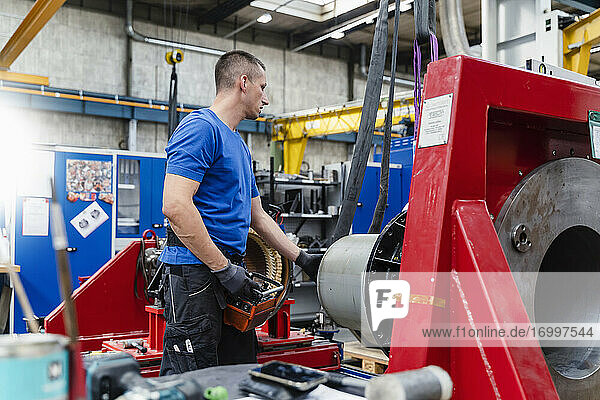 Male technician examining machine in illuminated industrial factory