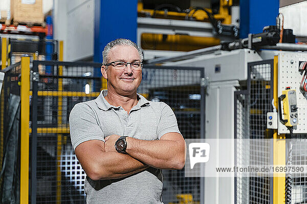 Confident male engineer with arms crossed standing in factory