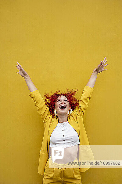 Überschwängliche junge Frau mit rotem lockigem Haar lachend vor einer gelben Wand