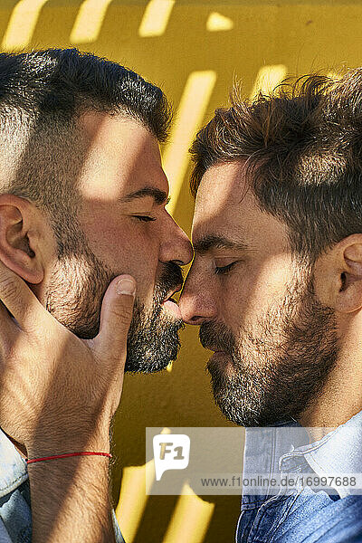 Gay couple doing romance while standing against yellow wall