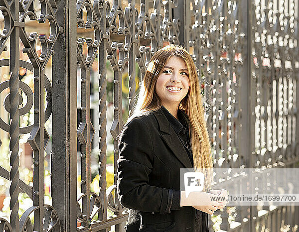 Young woman smiling while standing against gate