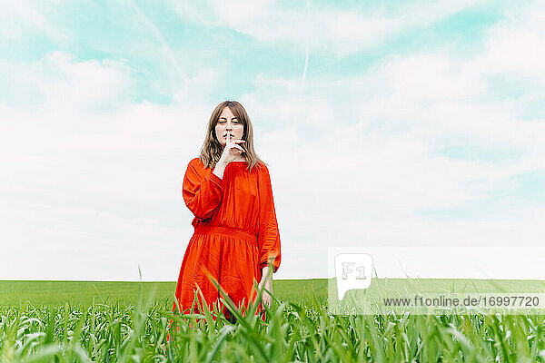 Porträt einer Frau in rotem Kleid  die in einem Feld steht und den Finger auf den Mund legt