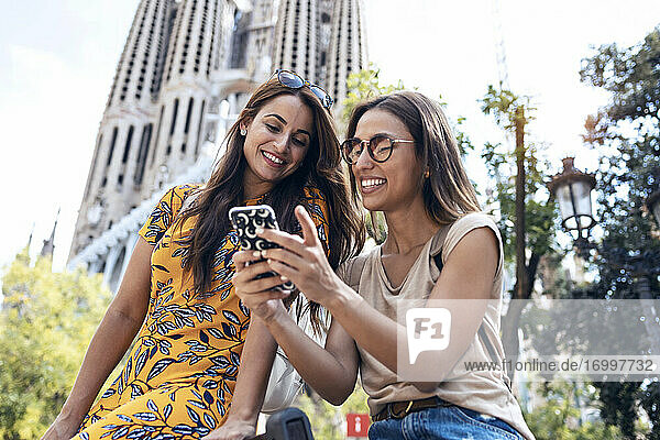 Frauen  die ein Mobiltelefon benutzen  während sie vor der Sagrada Familia in Barcelona  Katalonien  Spanien sitzen