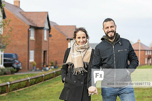 Smiling couple holding hands while standing outside new house