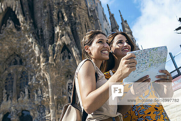 Lächelnde Freunde benutzen eine Landkarte  während sie vor der Sagrada Familia in Barcelona  Katalonien  Spanien stehen