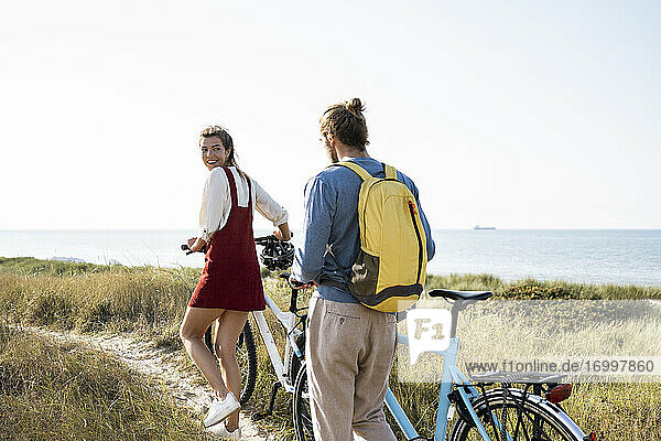 Young man and woman with bicycles walking on footpath against clear sky