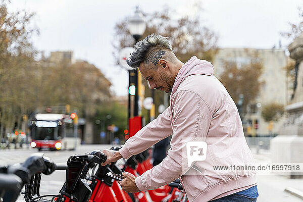 Stilvoller Mann  der ein Fahrrad über sein Smartphone an einer Parkstation ausleiht