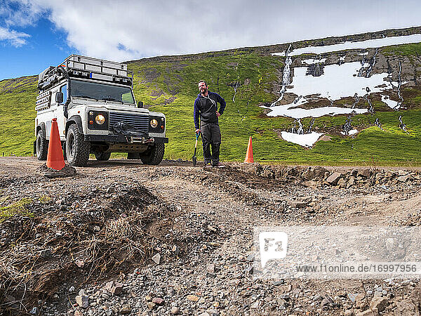 Man leaning on shovel in front of pot hole in middle of dirt road leading to Drangajokull
