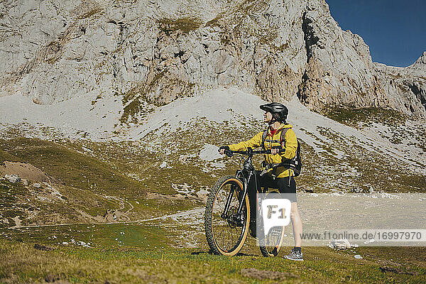 Woman with bicycle looking away against rock mountain on sunny day  Picos de Europa National Park  Cantabria  Spain